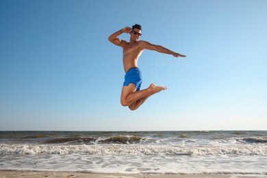 Photo of Attractive man with perfect body jumping on beach