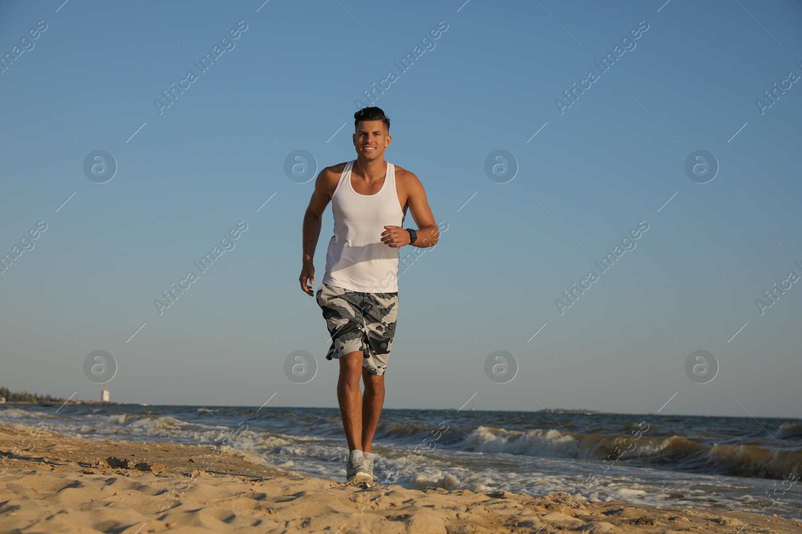 Photo of Sporty man running on sandy beach at sunset