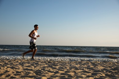 Photo of Sporty man running on sandy beach at sunset