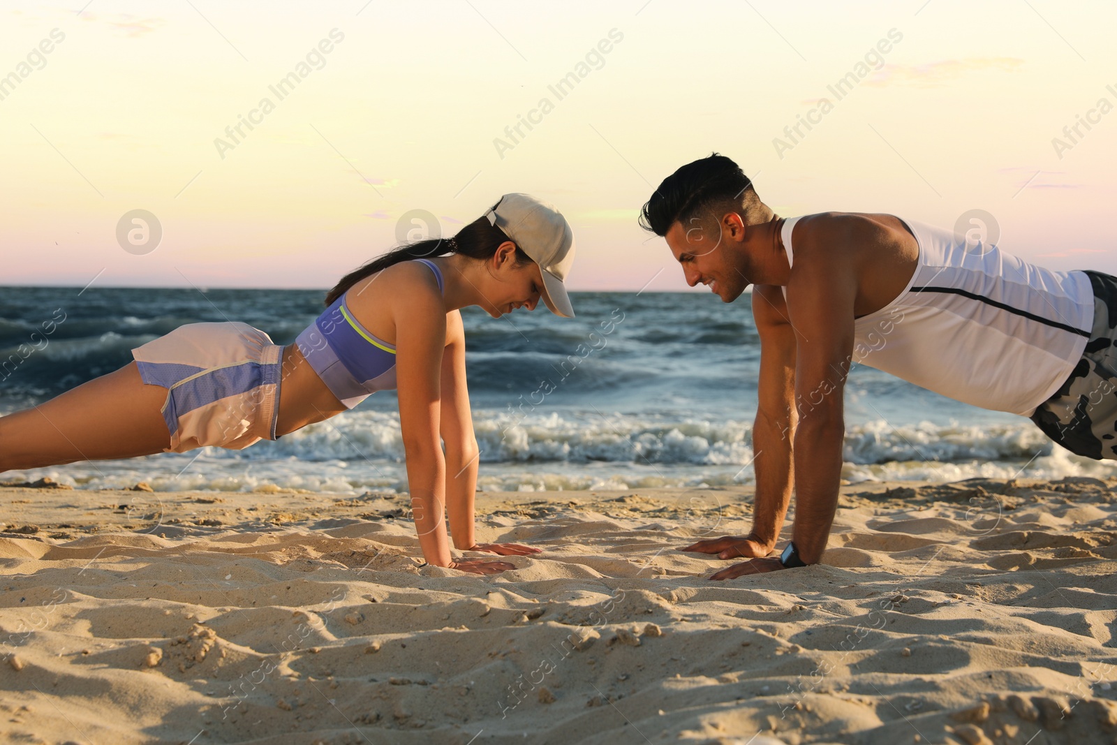 Photo of Sporty couple doing exercise on beach at sunset