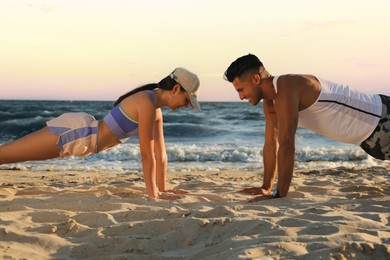 Photo of Sporty couple doing exercise on beach at sunset