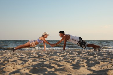 Photo of Sporty couple doing exercise on beach at sunset