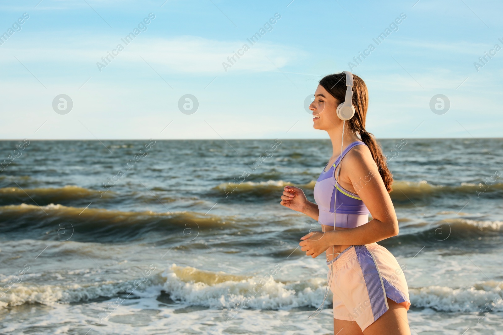 Photo of Young woman running on beach at sunset