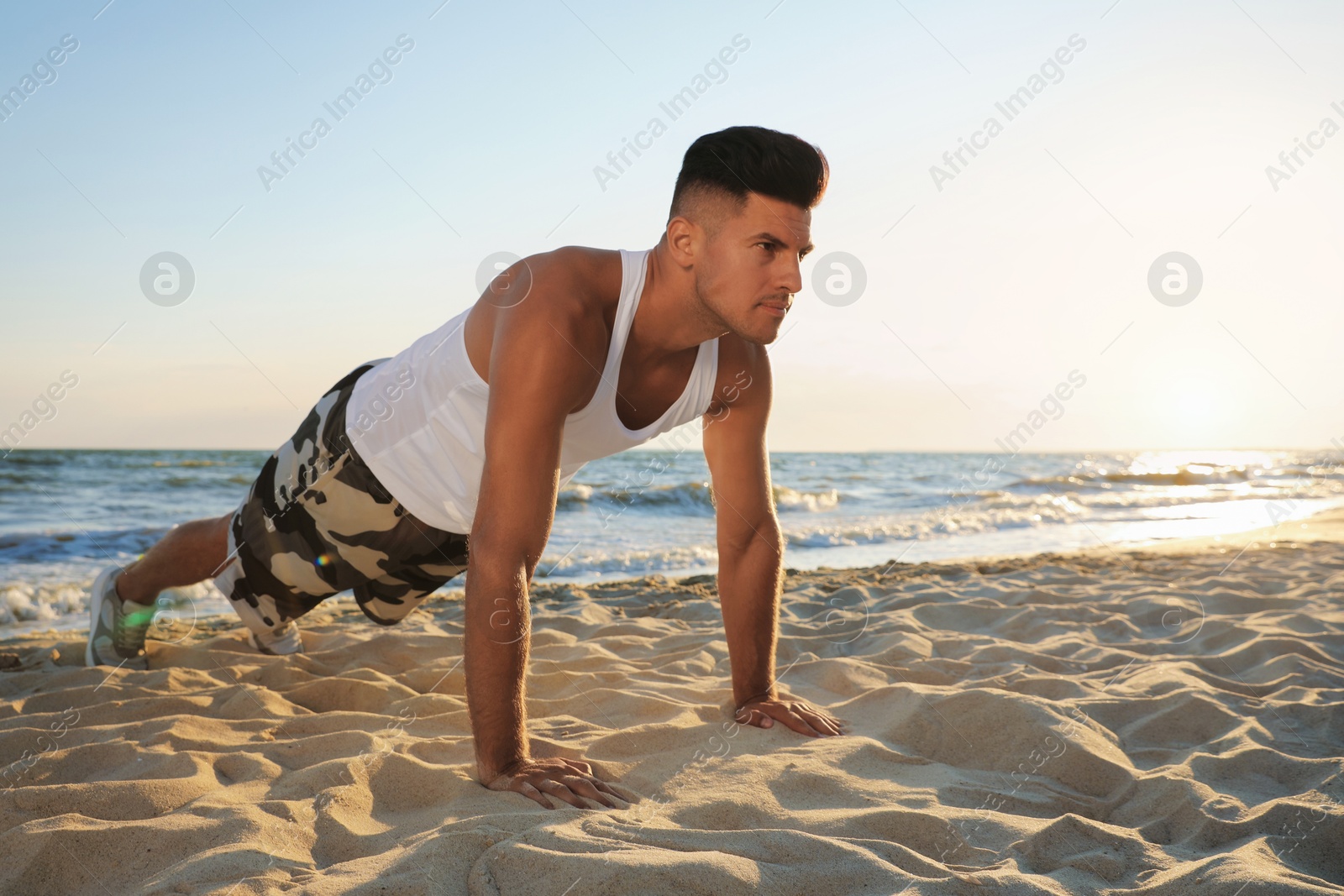 Photo of Sporty man doing plank on sandy beach