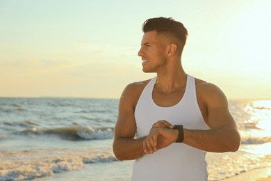 Photo of Man with athletic body checking fitness bracelet on beach