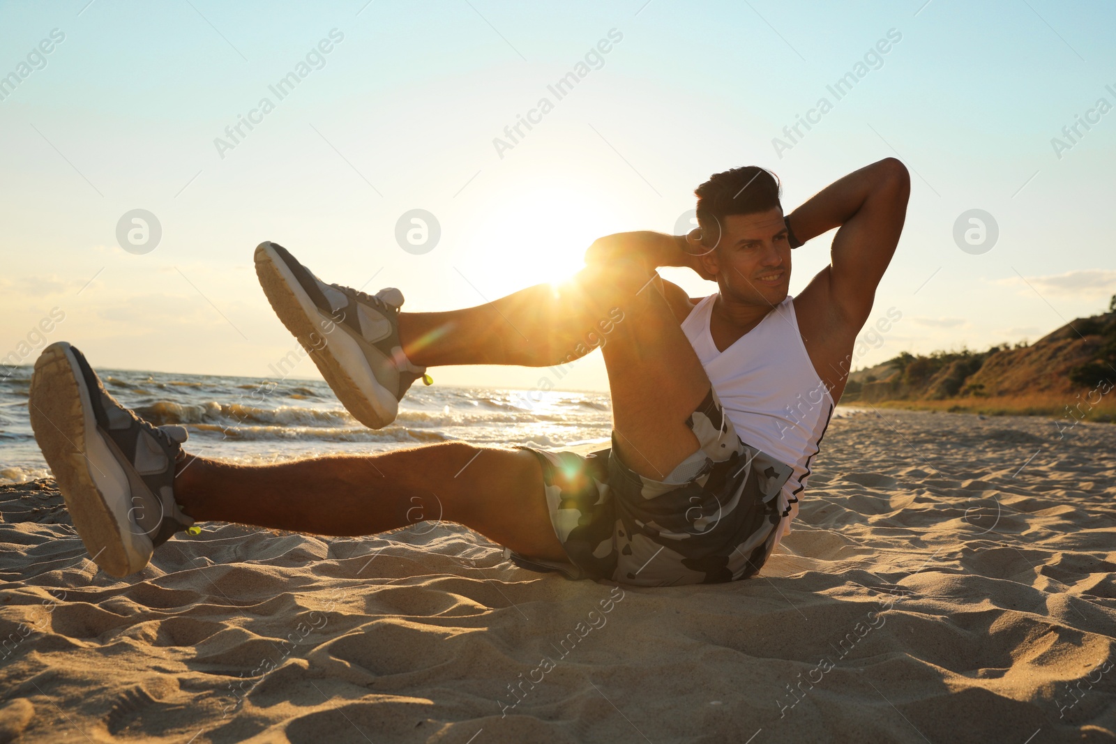 Photo of Sporty man with athletic body doing crunches on beach