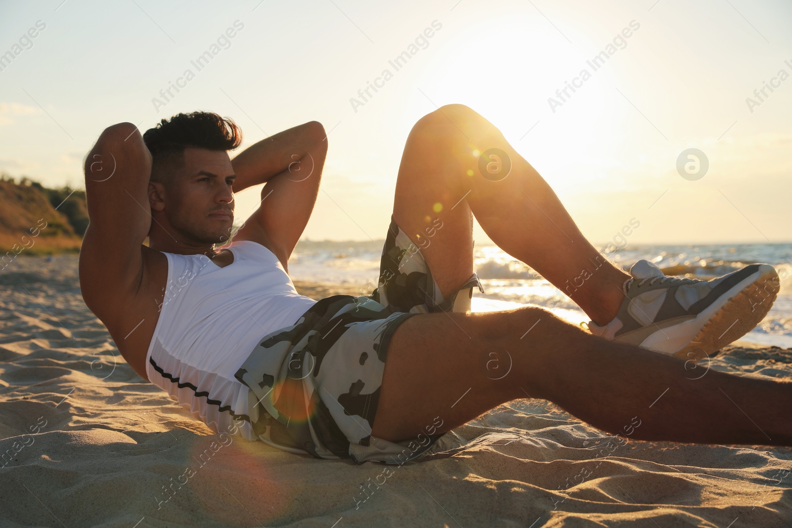 Photo of Sporty man with athletic body doing crunches on beach