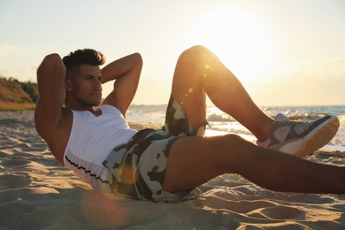 Photo of Sporty man with athletic body doing crunches on beach