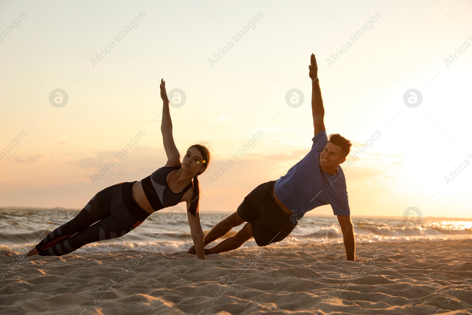 Photo of Couple doing yoga on beach at sunset