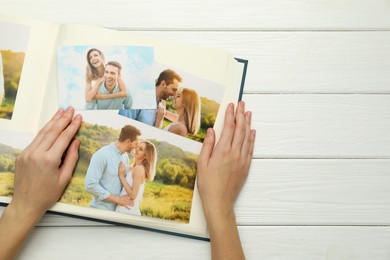 Photo of Woman with different photos in open photo album at white wooden table, top view. Space for text