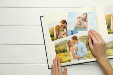 Photo of Woman with different photos in open photo album at white wooden table, top view. Space for text