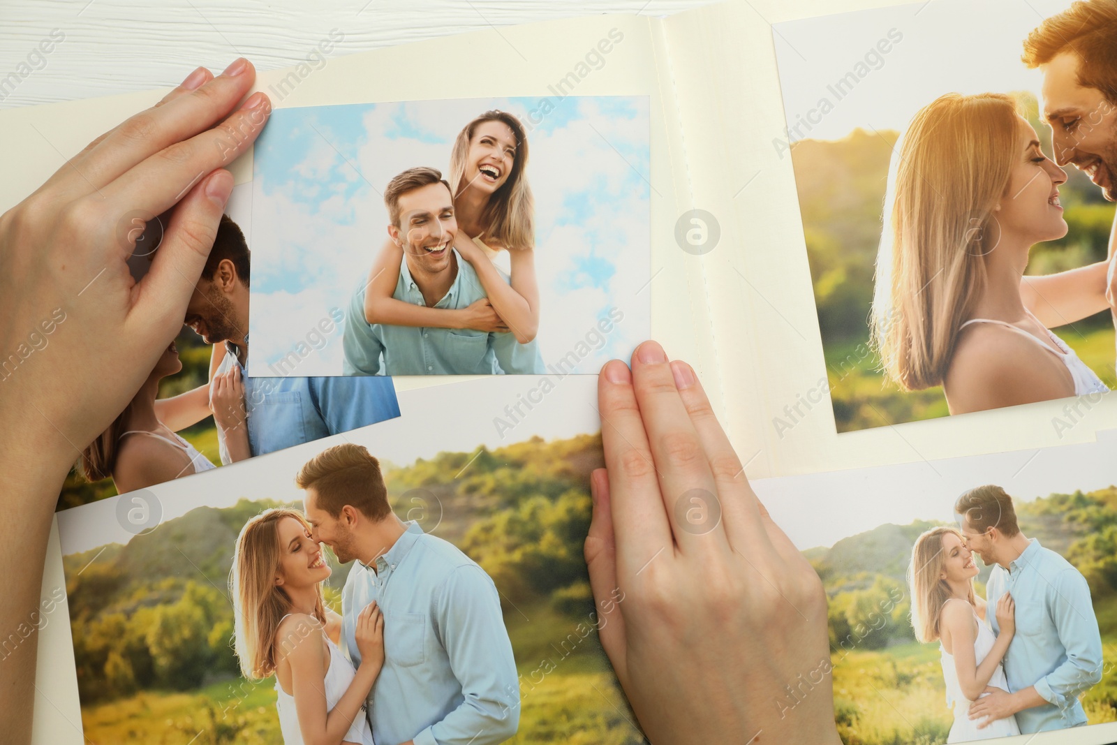 Photo of Woman with different photos in open photo album at white wooden table, top view