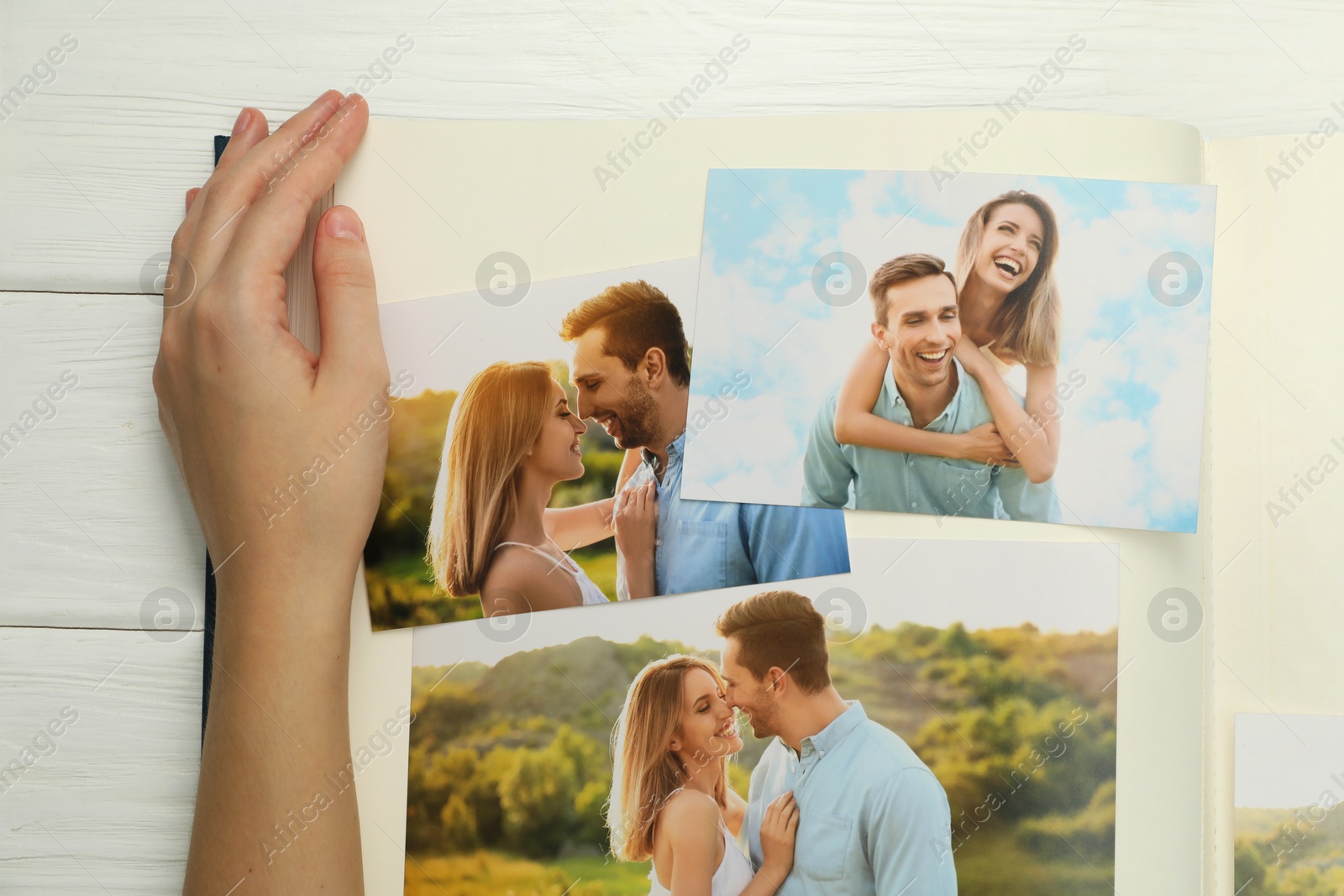 Photo of Woman with different photos in open photo album at white wooden table, top view