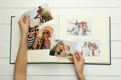 Photo of Woman with different photos in open photo album at white wooden table, top view