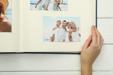 Photo of Woman with different photos in open photo album at white wooden table, top view