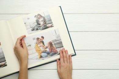 Photo of Woman with different photos in open photo album at white wooden table, top view. Space for text