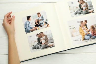 Photo of Woman with different photos in open photo album at white wooden table, top view