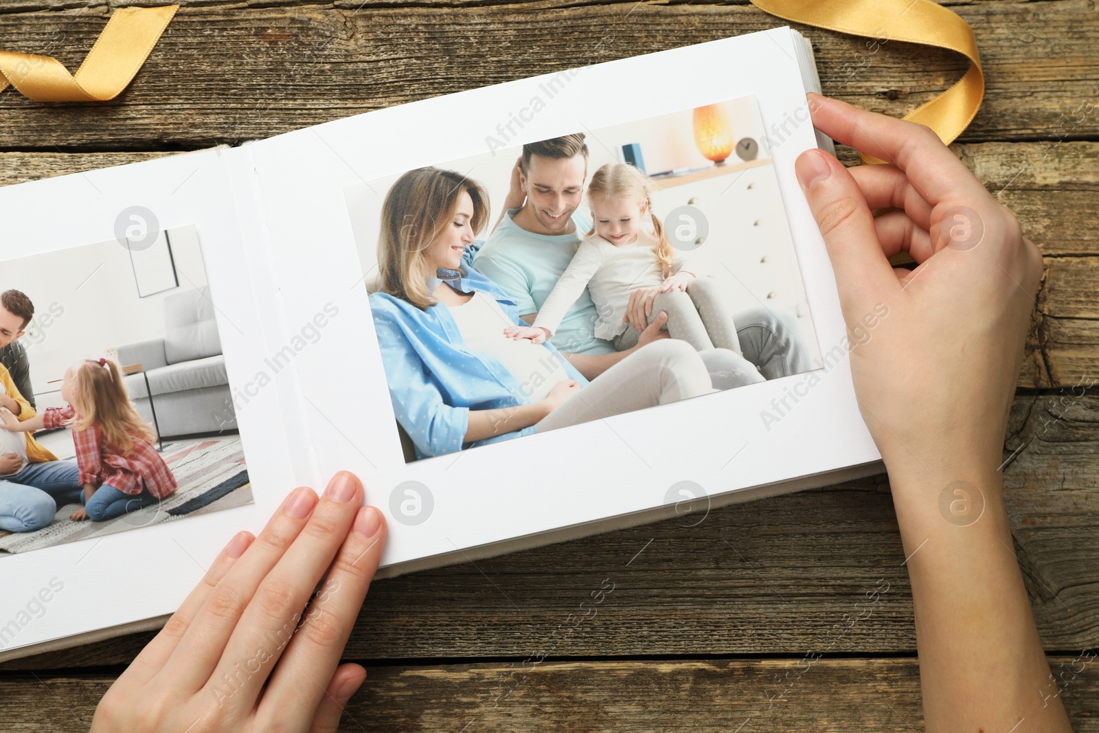 Photo of Woman with different photos in open photo album at wooden table, top view