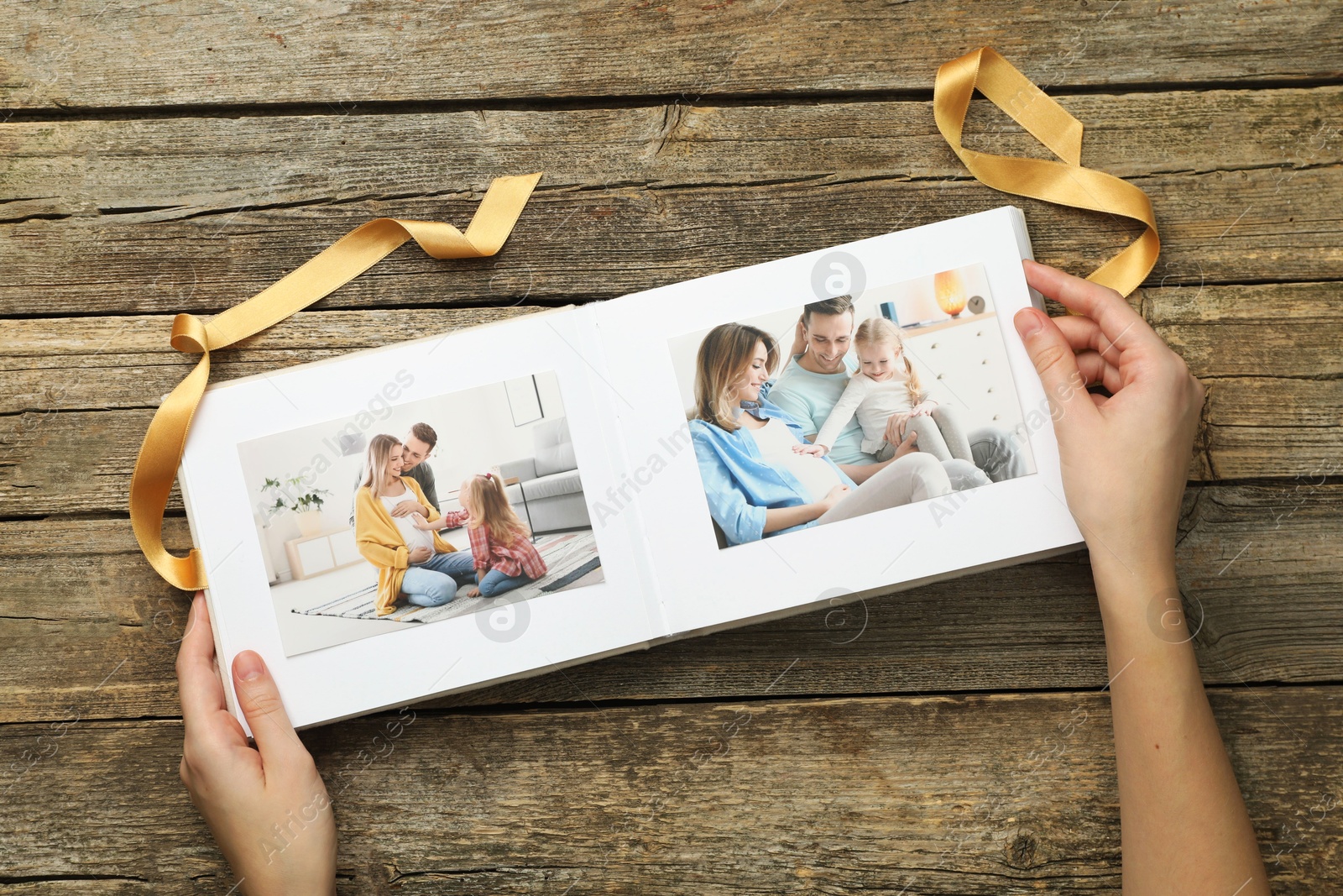 Photo of Woman with different photos in open photo album at wooden table, top view