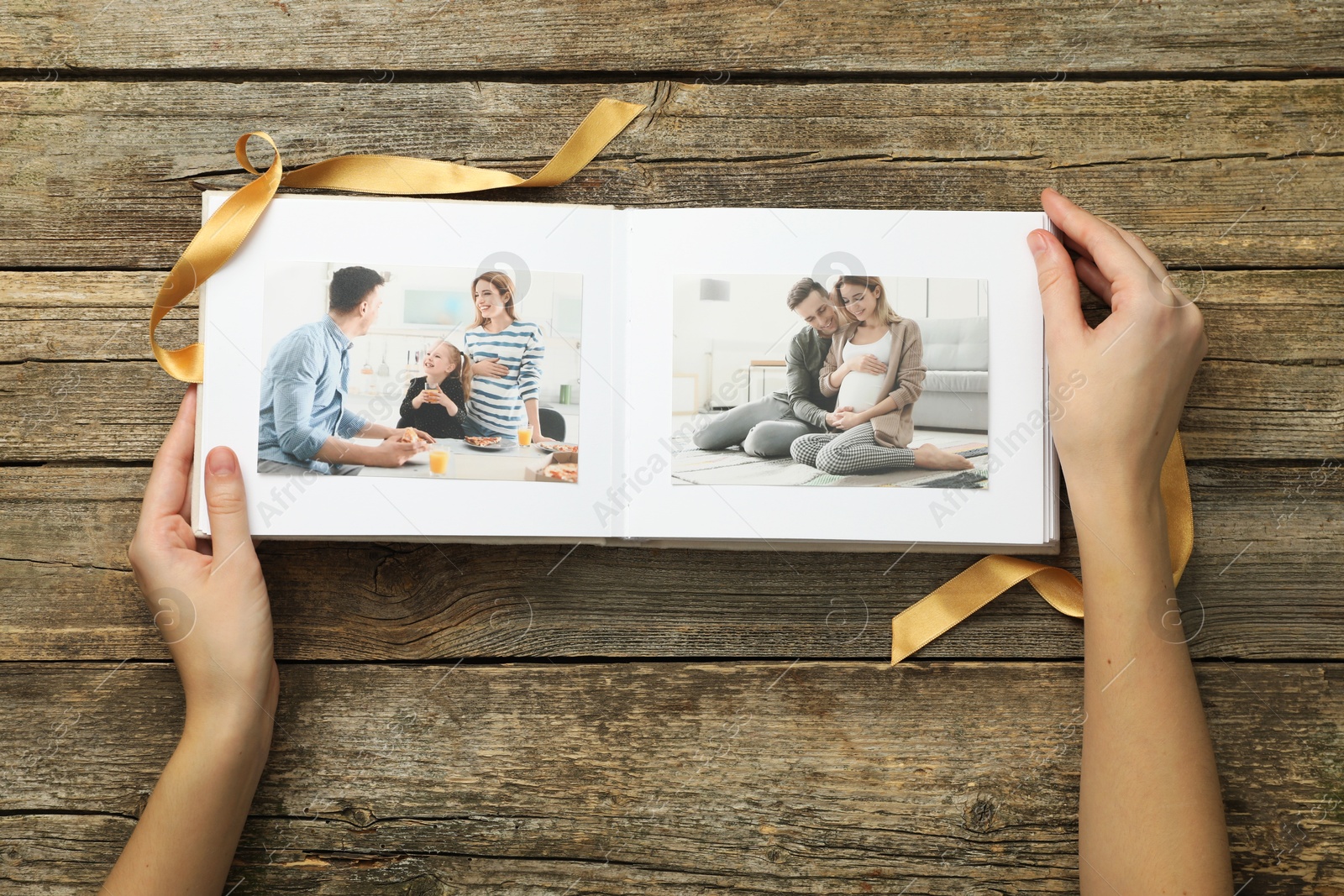 Photo of Woman with different photos in open photo album at wooden table, top view