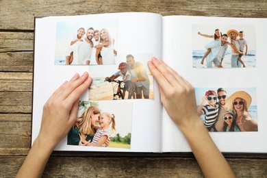 Photo of Woman with different photos in open photo album at wooden table, top view