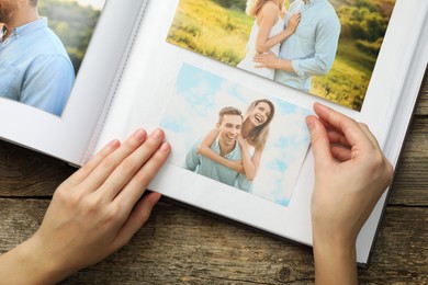 Photo of Woman with different photos in open photo album at wooden table, top view