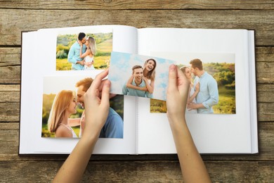 Photo of Woman with different photos in open photo album at wooden table, top view