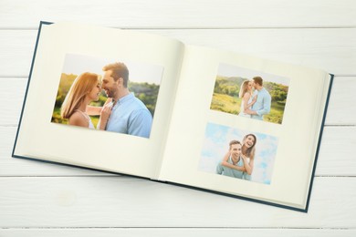 Photo of Different photos in open photo album on white wooden table, top view