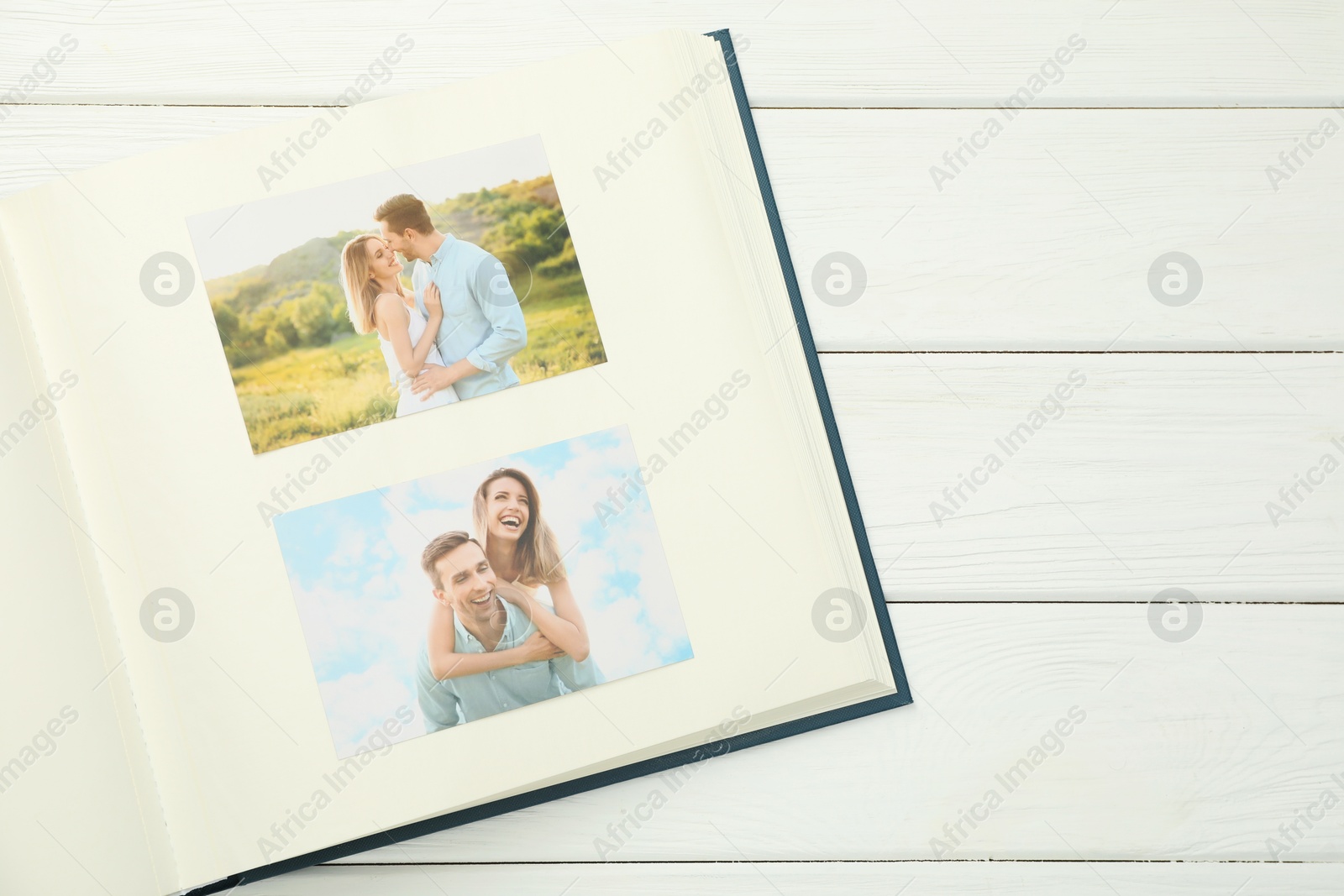 Photo of Different photos in open photo album on white wooden table, top view. Space for text