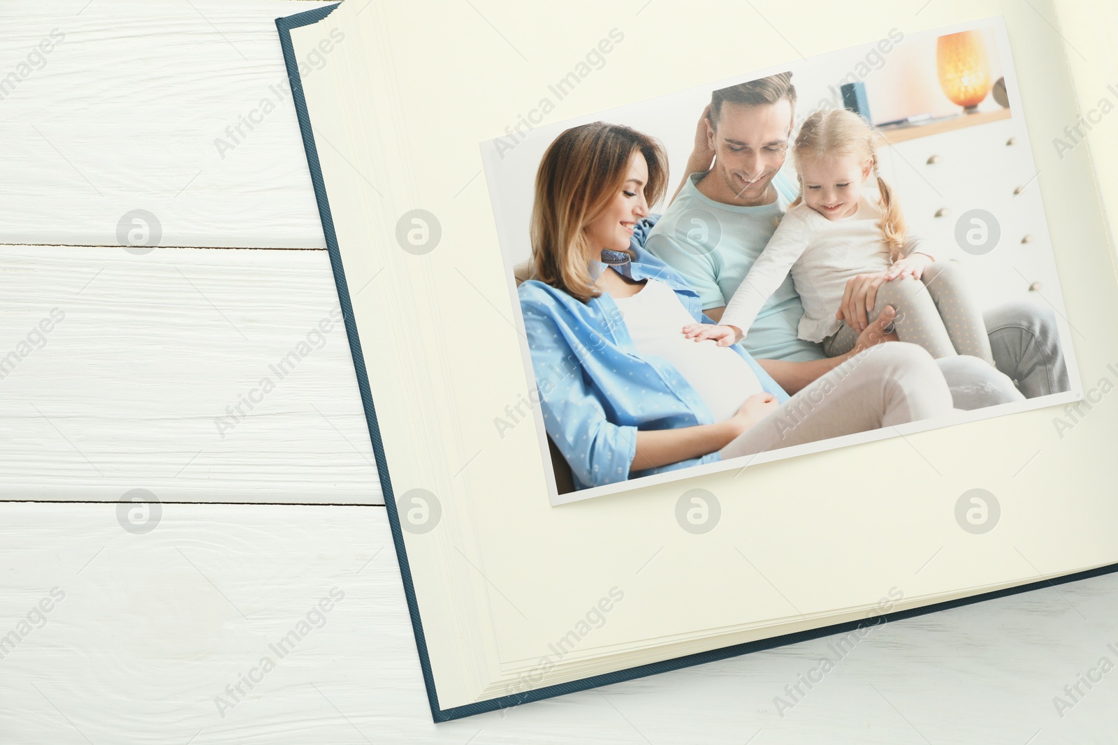 Photo of Different photos in open photo album on white wooden table, top view