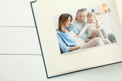 Photo of Different photos in open photo album on white wooden table, top view