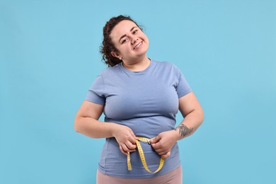 Photo of Weight loss. Happy plus size woman measuring waist with tape on light blue background