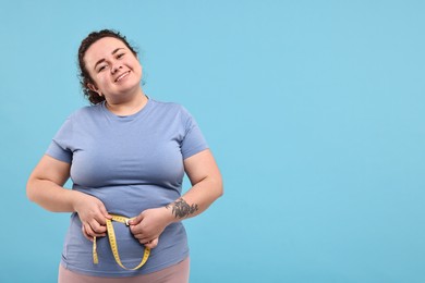 Photo of Weight loss. Happy plus size woman measuring waist with tape on light blue background, space for text