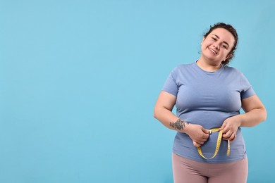 Photo of Weight loss. Happy plus size woman measuring waist with tape on light blue background, space for text