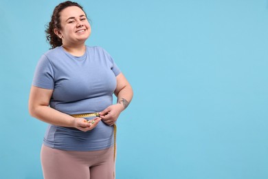 Photo of Happy plus size woman measuring waist with tape and holding pile of weight loss supplements on light blue background. Space for text