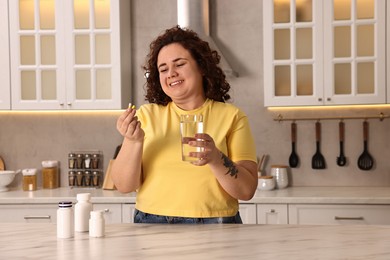 Photo of Happy plus size woman with weight loss supplements and glass of water at marble countertop in kitchen