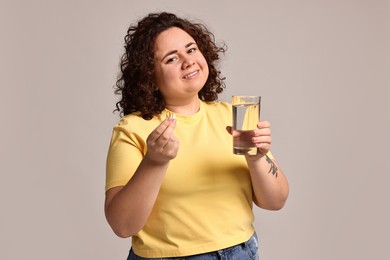 Photo of Happy plus size woman with weight loss supplements and glass of water on grey background