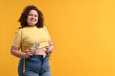 Photo of Happy plus size woman with blister of weight loss supplements on orange background. Space for text