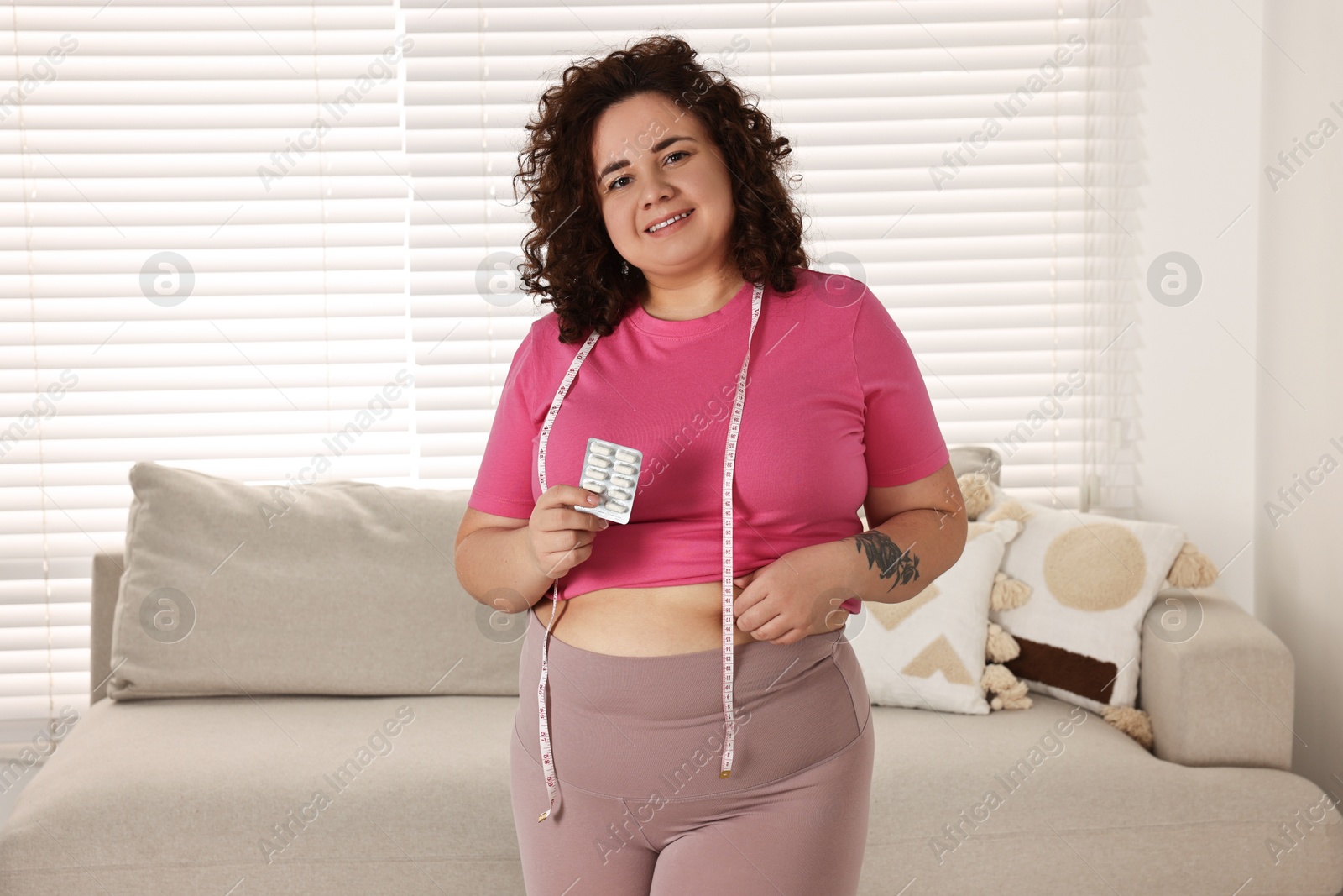 Photo of Happy plus size woman holding blister of weight loss supplements at home