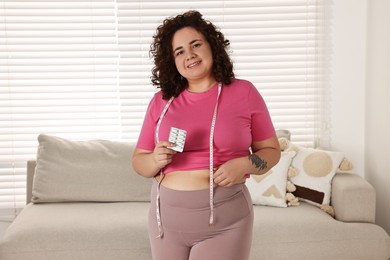 Photo of Happy plus size woman holding blister of weight loss supplements at home