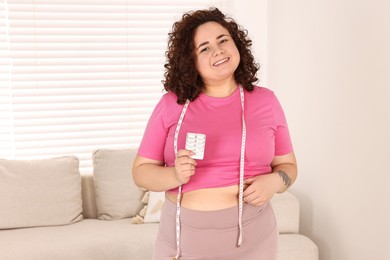 Photo of Happy plus size woman holding blister of weight loss supplements at home