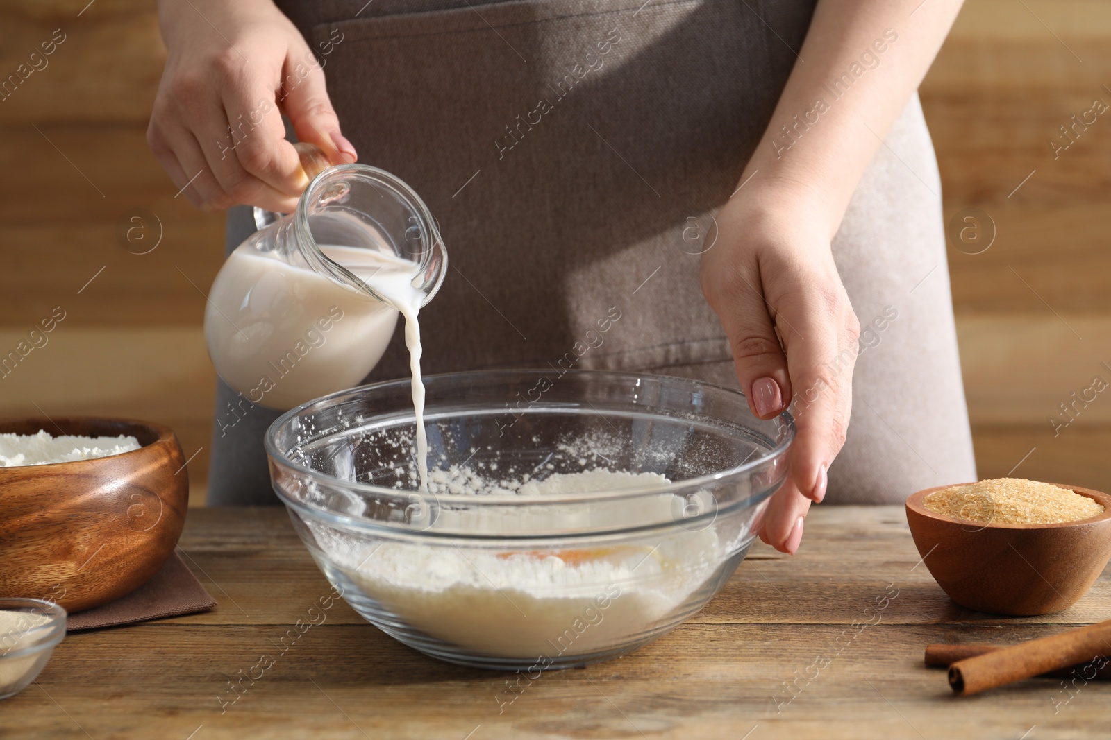 Photo of Making cinnamon rolls. Woman pouring milk into bowl at wooden table, closeup