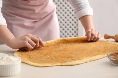 Photo of Making cinnamon rolls. Woman shaping dough at white table, closeup