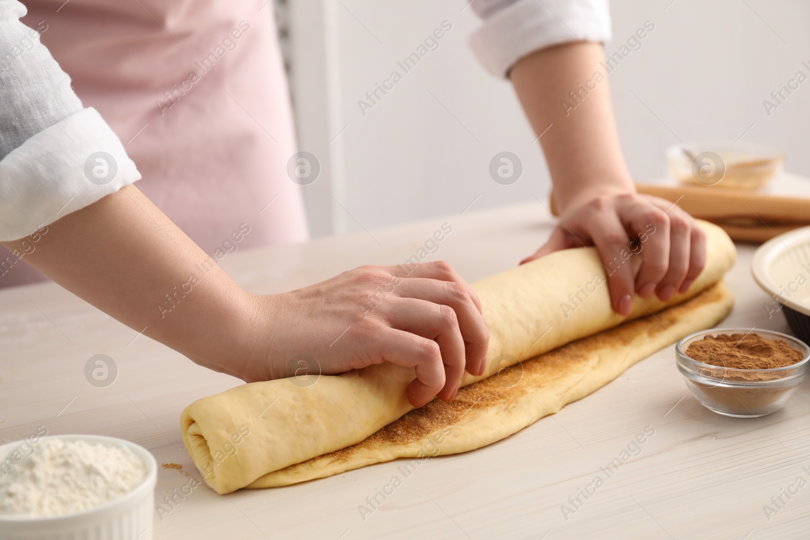 Photo of Making cinnamon rolls. Woman shaping dough at white wooden table, closeup