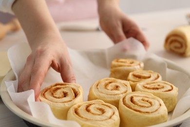 Photo of Woman putting cinnamon roll into baking dish at table, closeup