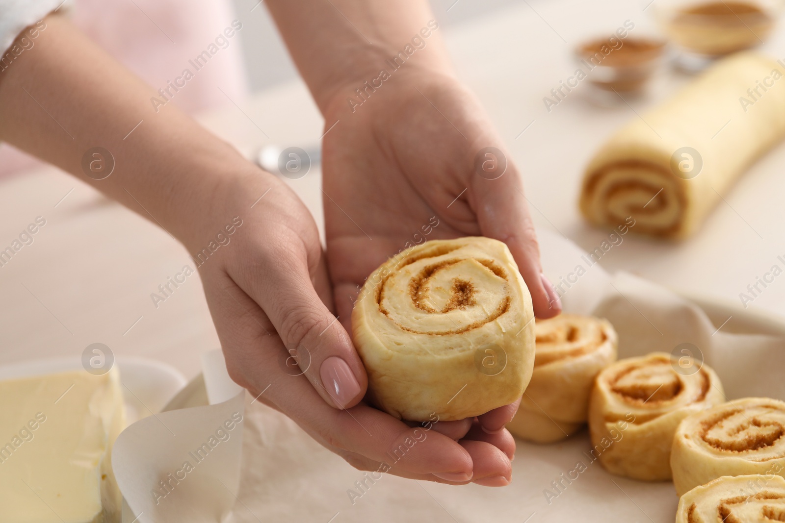 Photo of Woman putting cinnamon roll into baking dish at table, closeup