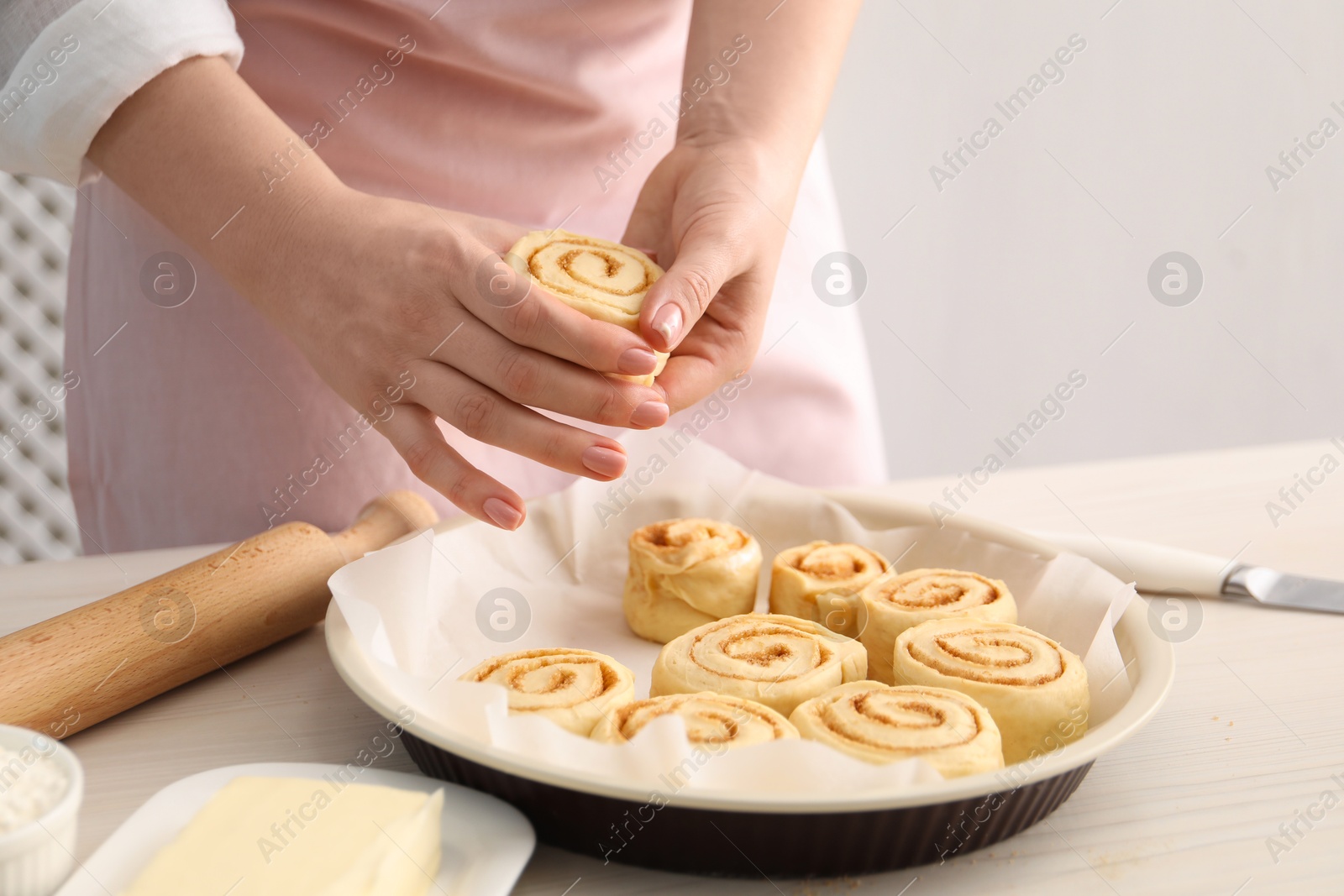 Photo of Woman making cinnamon rolls at white wooden table, closeup