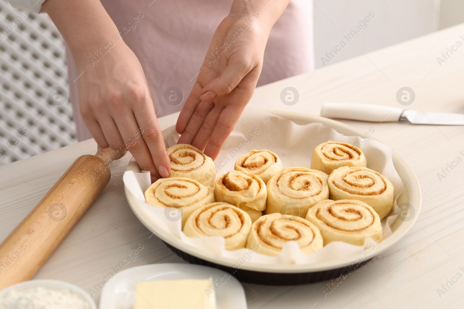 Photo of Woman making cinnamon rolls at white wooden table, closeup