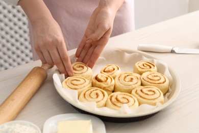 Photo of Woman making cinnamon rolls at white wooden table, closeup