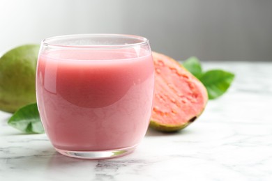 Photo of Tasty guava juice in glass, leaves and fruits on white marble table against grey background, closeup